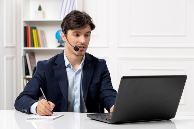 Kundenservice gutaussehender Typ mit Headset und Laptop im Anzug, der sich Notizen macht