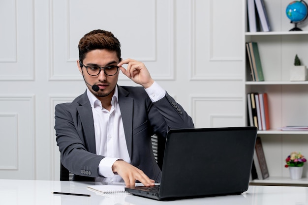 Kundenservice hübscher Herr mit Computer im grauen Büroanzug, der den Rand der Brille berührt