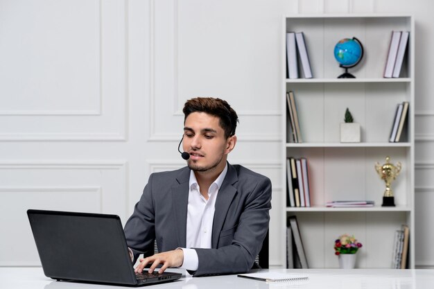Kundenservice intelligenter, gutaussehender Typ mit Laptop im grauen Büroblazer, der eine Anfrage tippt