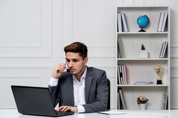 Kundenservice, intelligenter, gutaussehender Typ mit Laptop im grauen Büroblazer, der während des Anrufs spricht