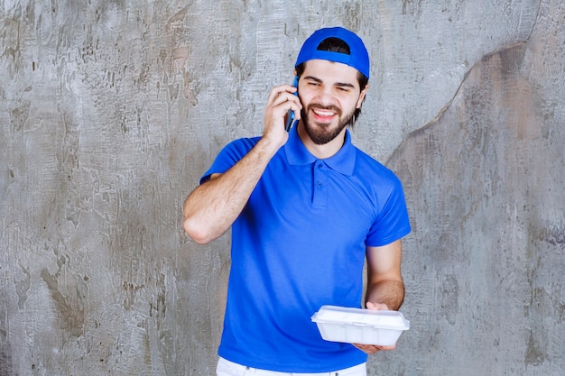 Kurier in blauer Uniform, der eine Plastikbox zum Mitnehmen hält und neue Bestellungen per Telefon entgegennimmt.