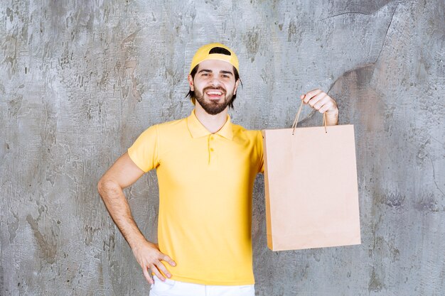 Kurier in gelber Uniform mit einer Einkaufstüte aus Pappe