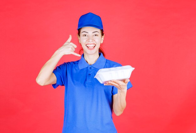 Kurierfrau in blauer Uniform, die eine weiße Box zum Mitnehmen hält und um einen Anruf bittet.