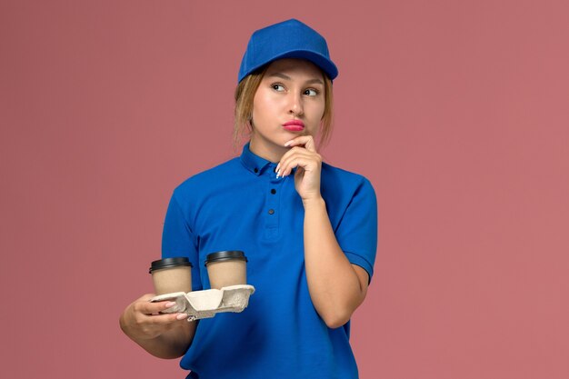 Kurierin in blauer Uniform, die Tassen Kaffee hält, die auf rosa, Dienstuniform-Lieferauftrag denken