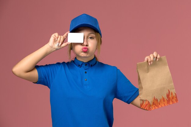 Kurierin in blauer Uniform mit weißer Plastikkarte und Lebensmittelverpackung auf rosa, Dienstuniform-Lieferauftrag