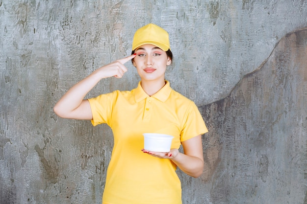 Kurierin in gelber uniform, die eine tasse zum mitnehmen hält, nachdenkt und eine gute idee hat