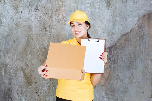 Kurierin in gelber Uniform liefert ein Papppaket und bittet um eine Unterschrift