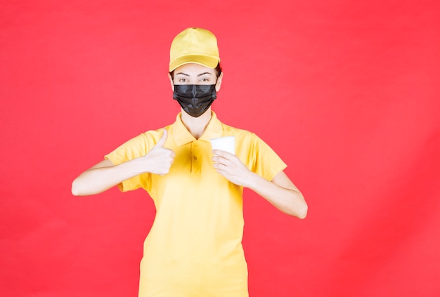 Kurierin in gelber Uniform und schwarzer Maske, die eine Tasse zum Mitnehmen hält und den Geschmack genießt