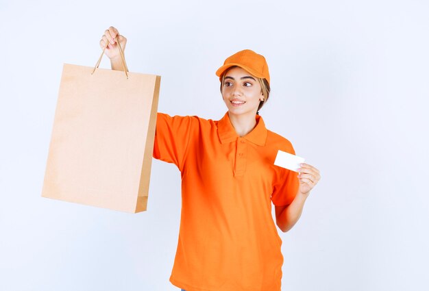 Kurierin in orangefarbener Uniform, die eine Einkaufstüte aus Pappe liefert und ihre Visitenkarte vorlegt