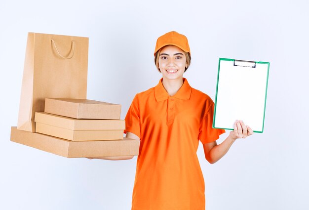 Kurierin in orangefarbener Uniform, die einen Vorrat an Papppaketen und Einkaufstüten hält und dem Kunden die Unterschriftenliste vorlegt