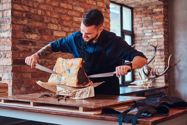 Lachend durchbohrt der Koch mit Messern exklusives Jerky-Fleisch in einer Küche mit Loft-Interieur.