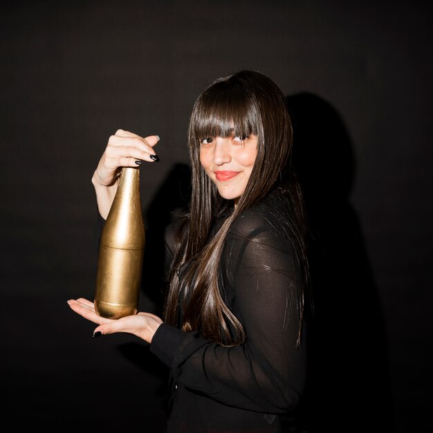 Lachende Brunettefrau in der Abendkleidung mit Flasche des Getränks