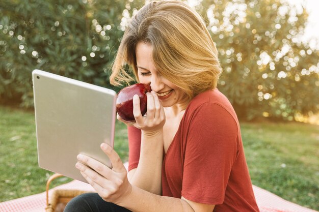 Lachende Frau mit Apfel mit Tablet