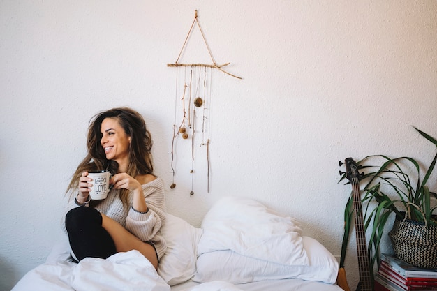 Lachende Frau mit Kaffee auf dem Bett