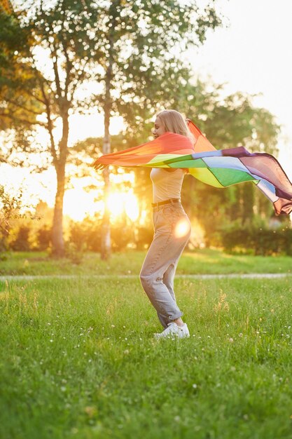 Lachende Frau tanzt mit LGBT-Flagge hinter dem Rücken