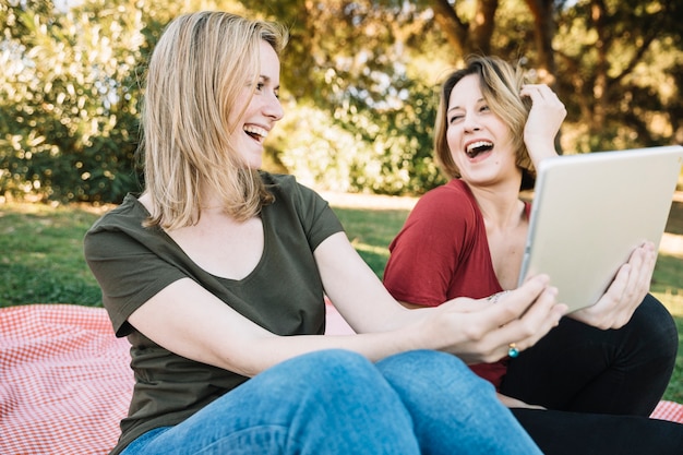 Lachende Frauen, die Tablette im Park verwenden