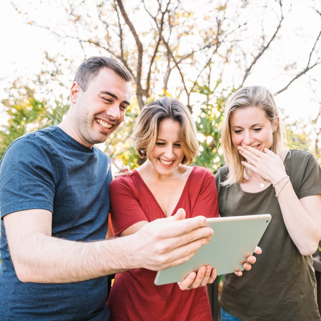 Lachende Freunde, die Tablette im schönen Park verwenden