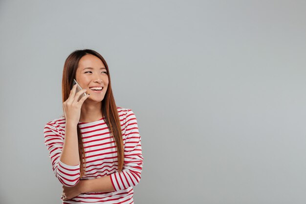 Lachende junge asiatische Frau, die per Telefon spricht