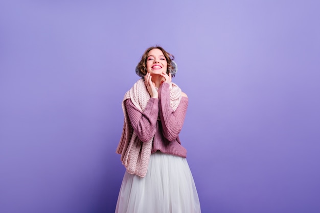 Lachende kaukasische Dame im Winterzubehör, das Fotoshooting genießt. Prächtiges weißes Mädchen im üppigen Vintagen Rock, der in lila Wand aufwirft.