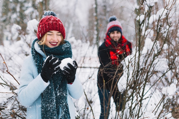 Lachende Paare, die Schneebälle im Holz spielen