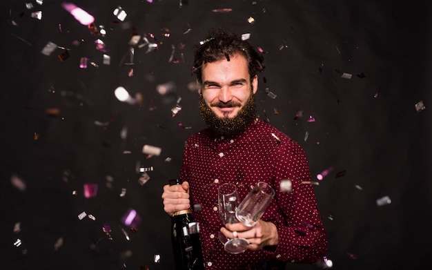 Lachender Kerl mit Flasche und Gläsern zwischen Konfetti