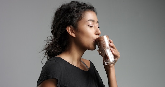 Kostenloses Foto lachendes attraktives mädchen aus dem nahen osten in entspanntem schwarzem oberteil, das mokka-coffee-coffee aus einem hohen glas trinkt, isoliert auf grau