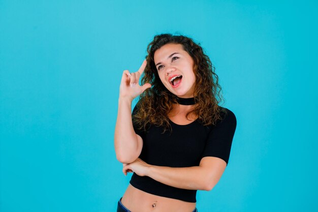 Lachendes Mädchen zeigt mit dem Zeigefinger auf blauem Hintergrund nach oben