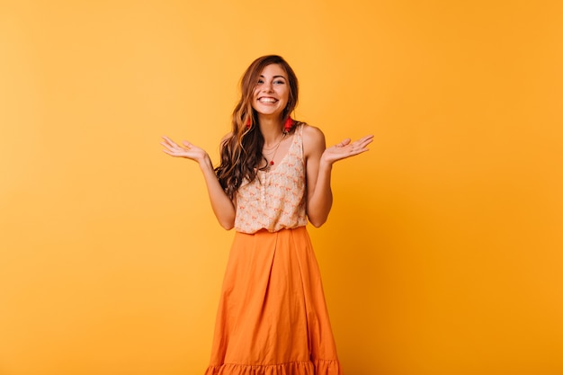 Lachendes optimistisches Mädchen mit langer Frisur, die auf Orange steht. Scherzhafte Dame mit welligem Haar, die das Leben genießt.