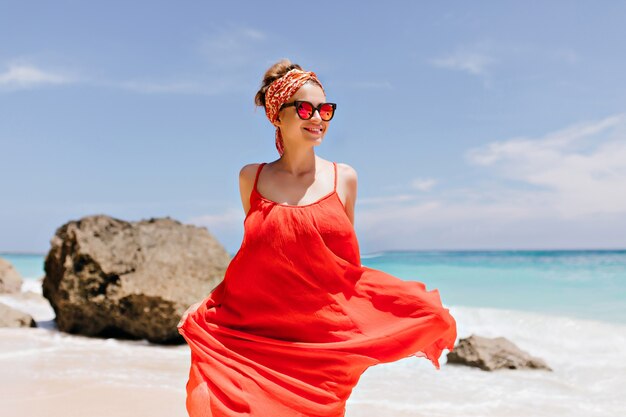 Lachendes weißes Mädchen, das am sonnigen Wochenende am Strand herumalbert. Foto im Freien der kaukasischen romantischen Dame im trendigen Kleid, das mit Steinen tanzt.