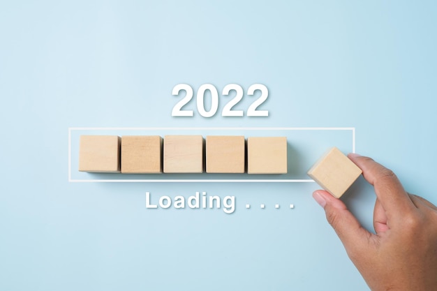 Laden des neuen jahres 2021 bis 2022 mit der hand, die den holzwürfel im fortschrittsbalken auf blauem hintergrund platziert