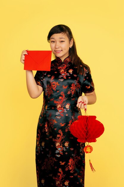 Lächeln mit Laterne und Umschlag. Frohes chinesisches neues Jahr 2020. Porträt des asiatischen jungen Mädchens auf gelbem Hintergrund. Weibliches Modell in traditioneller Kleidung sieht glücklich aus. Feier, Emotionen. Copyspace.