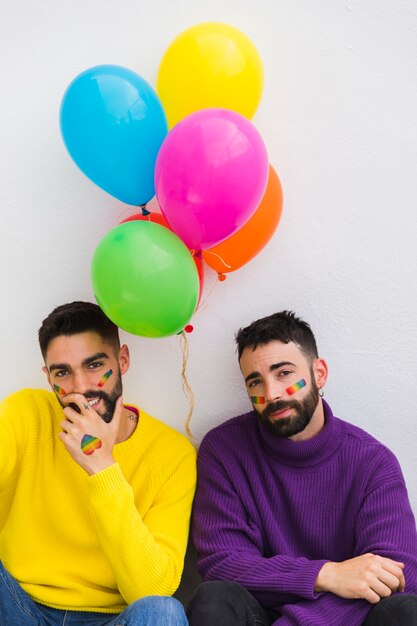 Lächeln und müde Homosexuelle sitzen mit Ballons