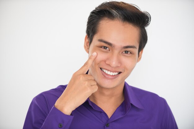 Lächelnd Junger hübscher asiatischer Mann, der zum Auge zeigt