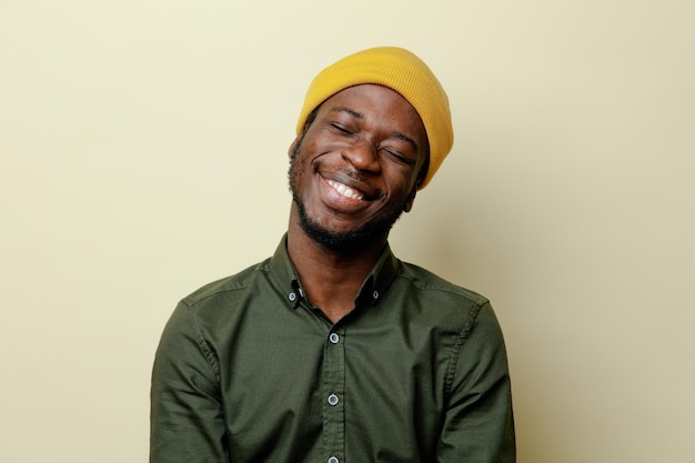 Lächelnd mit geschlossenen Augen junger afrikanisch-amerikanischer Mann mit Hut und grünem Hemd auf weißem Hintergrund