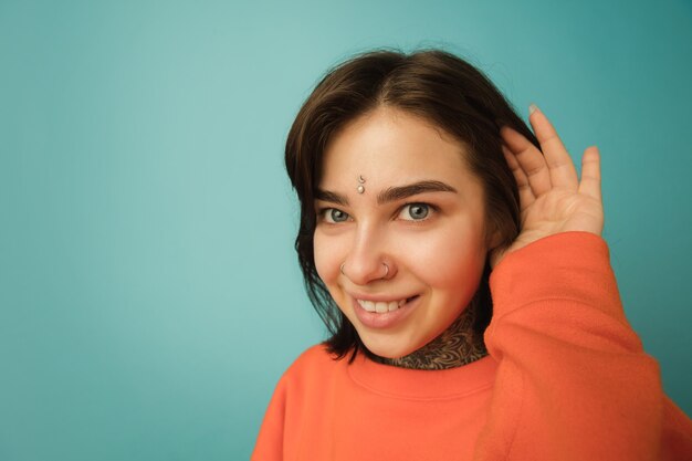 Lächelnd, Nahaufnahme. Porträt der kaukasischen Frau isoliert auf blauer Wand mit Exemplar. Schönes weibliches Modell im orangefarbenen Hoodie. Konzept der menschlichen Emotionen, Gesichtsausdruck,