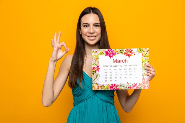 Lächelnd zeigt schöne Geste schöne junge Mädchen am glücklichen Frauentag mit Kalender