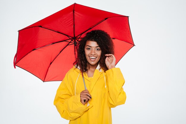 Lächelnde afrikanische Frau im Regenmantel, der mit Regenschirm aufwirft