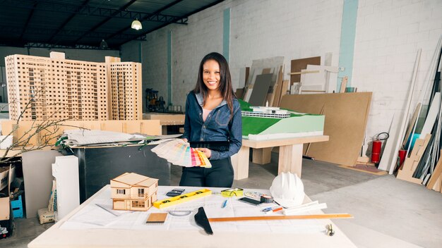Lächelnde Afroamerikanerfrau mit Beispielen von Farben nähern sich Tabelle mit Ausrüstungen