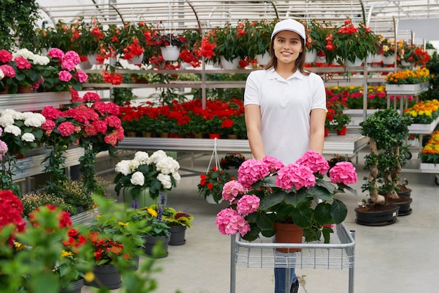 Lächelnde Arbeiterin mit Blumen im Gewächshaus
