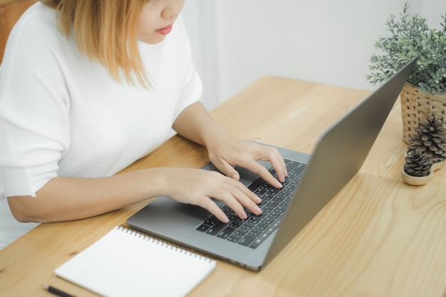 Lächelnde Asiatin der schönen Junge, die an Laptop während zu Hause im Büroarbeitsplatz arbeitet