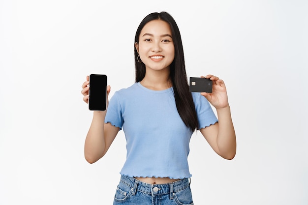 Lächelnde asiatische frau, die handybildschirm mit kreditkartenkonzept des onlineeinkaufs und der bestellung zeigt