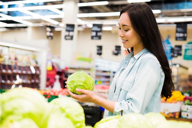 Lächelnde asiatische Frau, die Kohl im Markt wählt