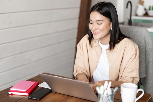 Lächelnde asiatische Nachhilfelehrerin, die Unterricht an einer Online-Sprachschule mit Laptop zur Arbeit...