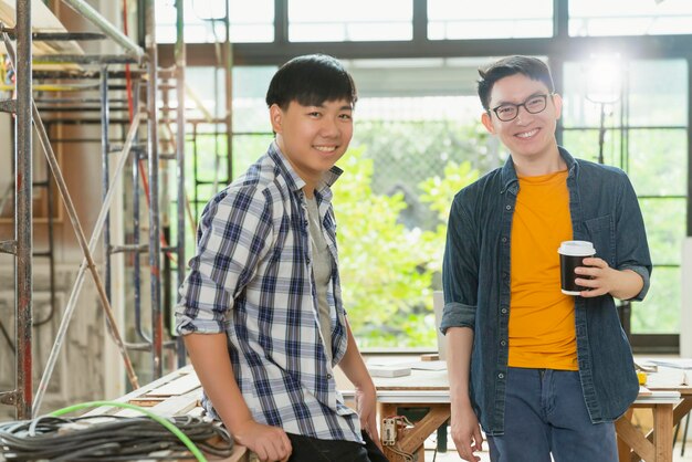 Lächelnde asiatische Teamarbeit junger Innendesigner-Porträts stehen zusammen, Handbrust, selbstbewusstes und intelligentes Team mit Hintergrund der Baurenovierung