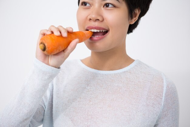 Lächelnde attraktive asiatische Frau beißt Karotte