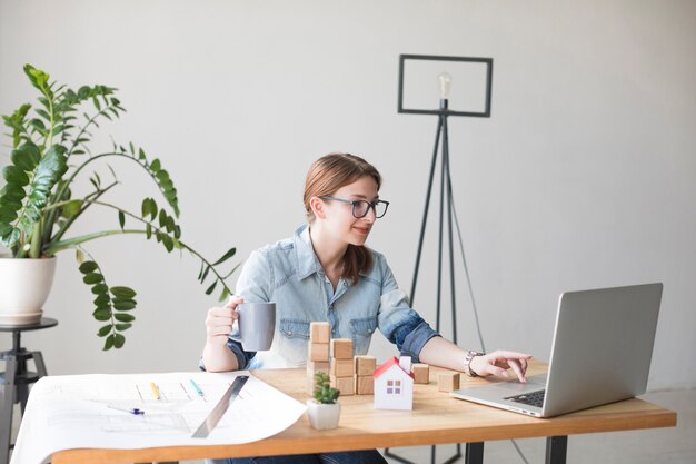 Lächelnde attraktive Frau, die Kaffeetasse beim Arbeiten an Laptop hält