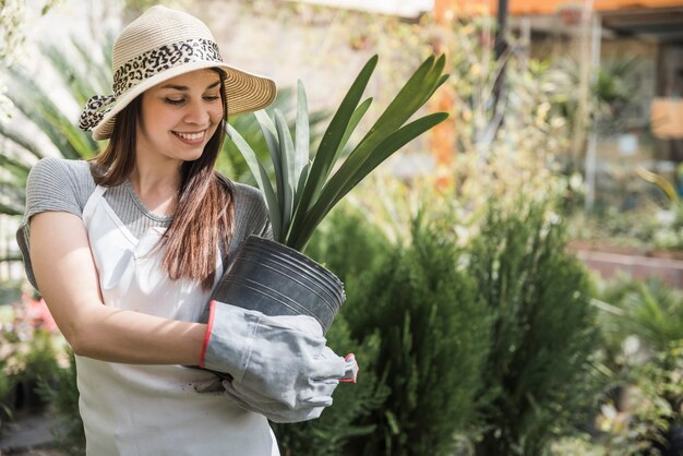 Lächelnde attraktive junge Frau an einer Blumenkindertagesstätte, die eine Topfpflanze hält