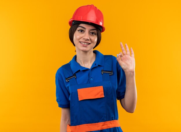 Lächelnde Blick in die Kamera junge Baumeisterin in Uniform, die eine gute Geste zeigt