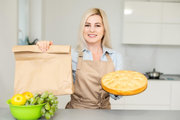 Lächelnde blonde frau, die eine schachtel mit hausgemachten dekorierten keksen in der küche hält. geschenk, kleinunternehmen, lieferung von süßigkeiten konzept