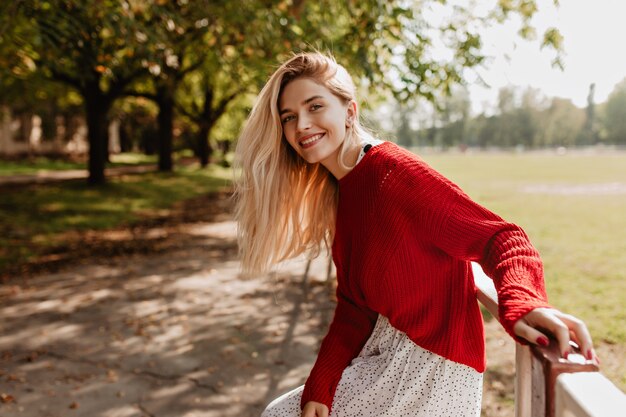 Lächelnde blonde Frau, die fröhlich auf der Straße lacht. Schöne junge Dame, die sich im Herbstpark glücklich fühlt.